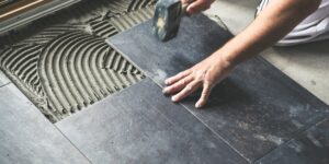 Close-up of a skilled worker's hands carefully laying dark slate tiles onto a freshly applied adhesive, exemplifying meticulous home remodel planning and installation precision