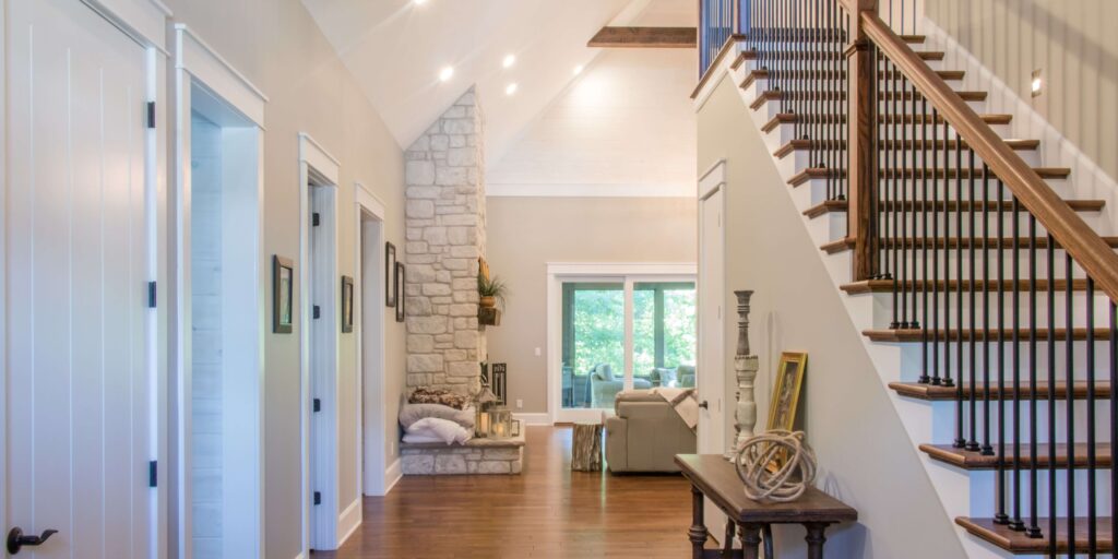A spacious hallway of a whole house remodel with gleaming hardwood floors, white paneled doors, a stone accent wall, and an elegant wooden staircase leading to the upper level, conveying a bright and modern home interior.